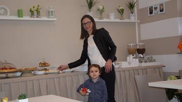 Una mujer de pie junto a una mesa de buffet con un niño que sostiene un juguete.