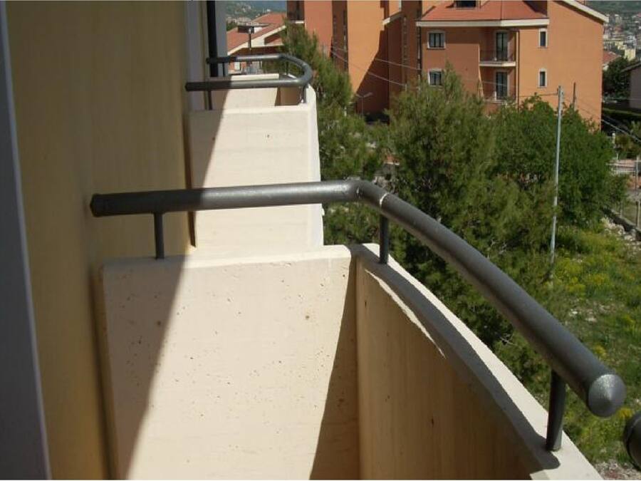 Un balcon doté d’une rambarde en métal et d’un mur de couleur beige.