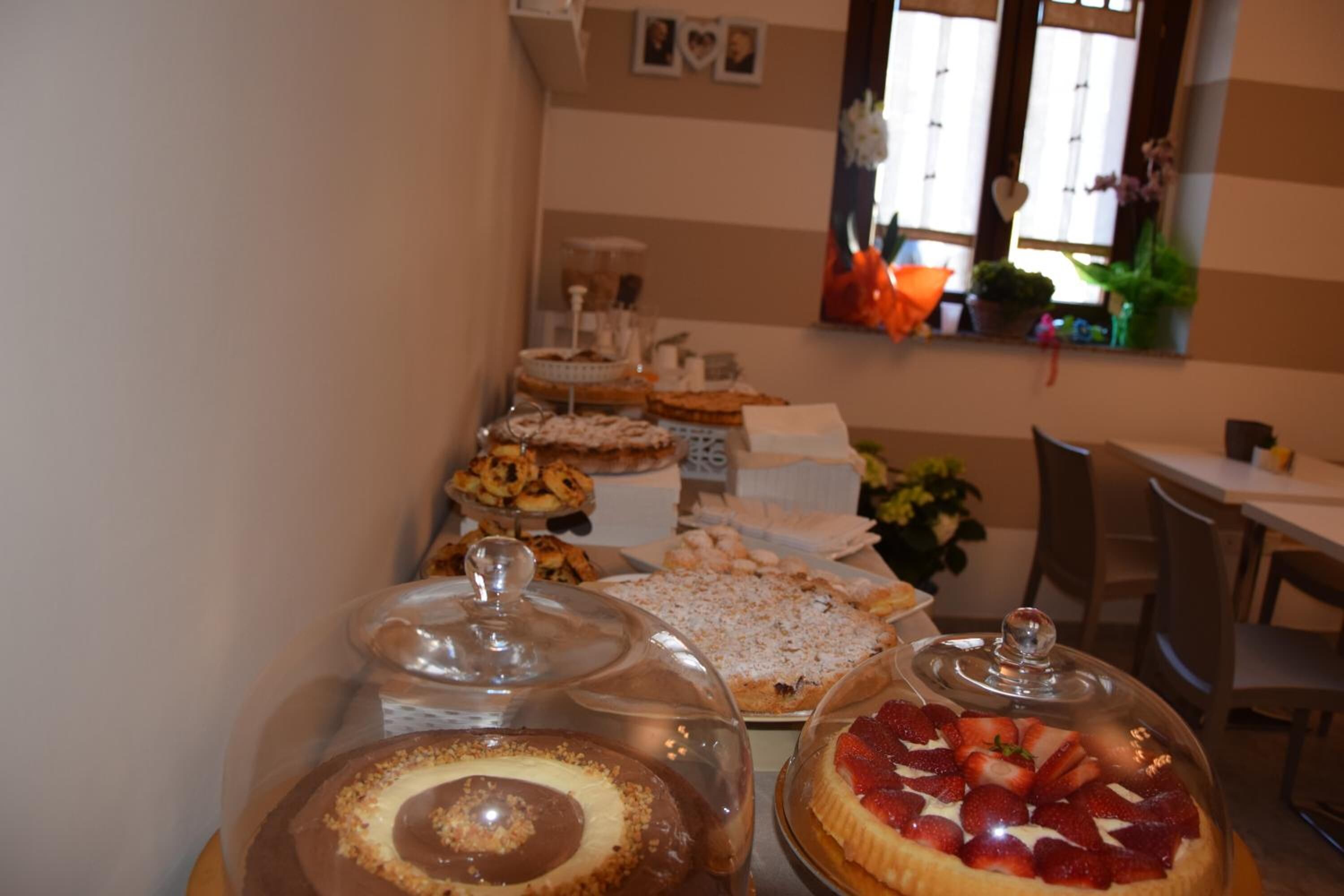 A buffet with various desserts under glass covers, a window with plants, and a striped wall.