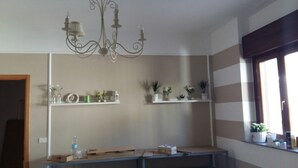A room with a chandelier, two shelves with plants, a window with blinds, and a door. - Hotel dei Cappuccini (San Giovanni Rotondo)