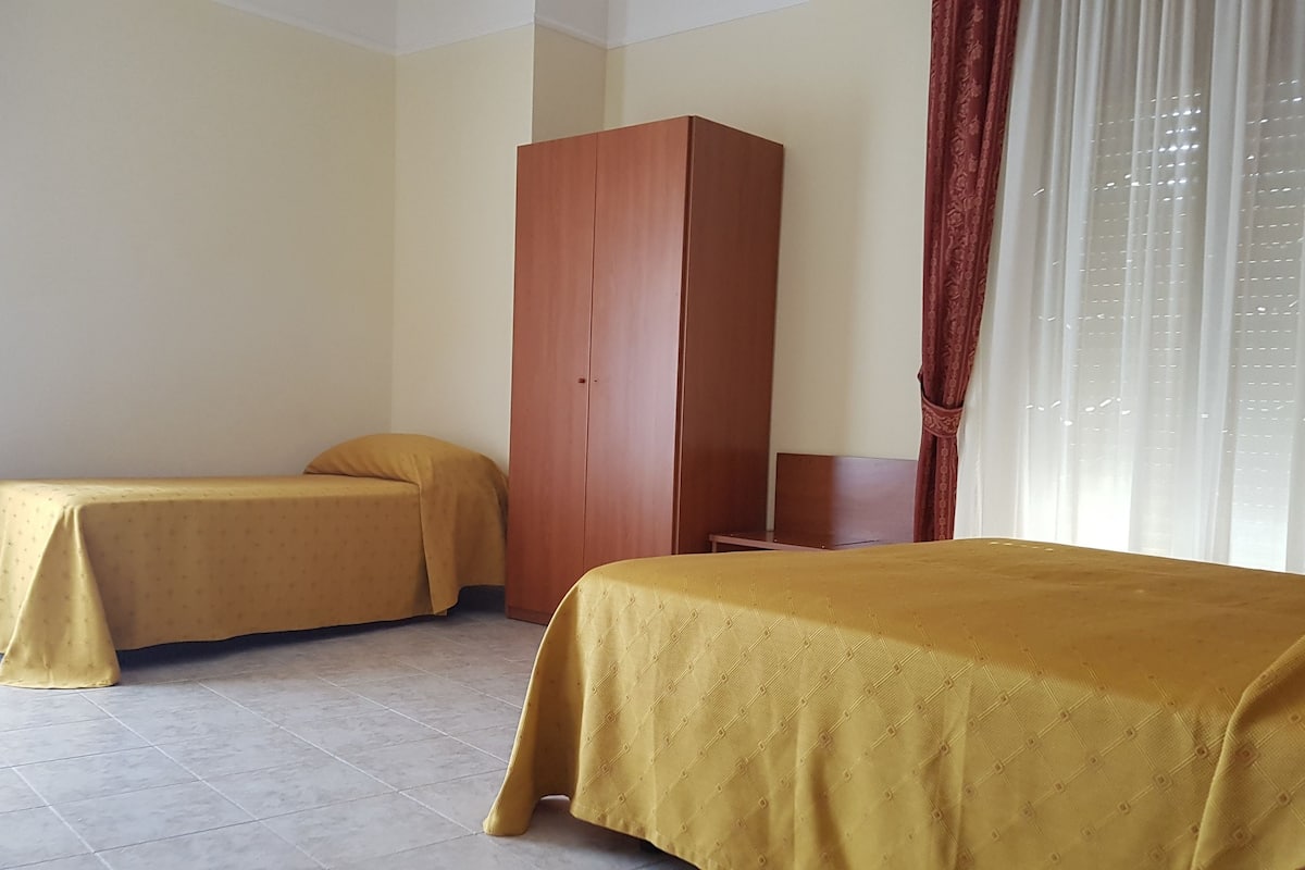 Een hotelkamer met twee enkele bedden, een garderobe en een raam met gordijnen.