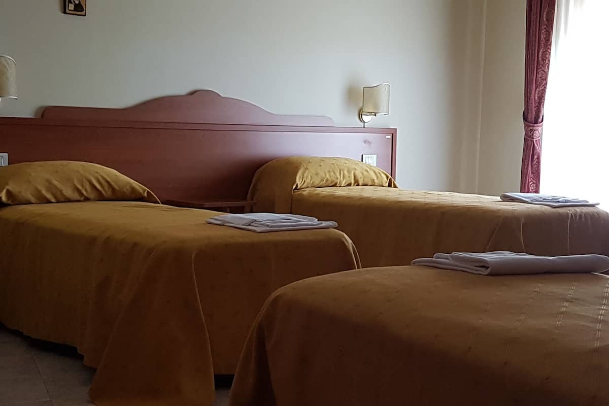 Een hotelkamer met twee eenpersoonsbedden, elk met hoofdbord en nachtkastje. Aan de linkerzijde van het bed hangt een wandlamp en aan de rechterzijde een raam met gordijnen.