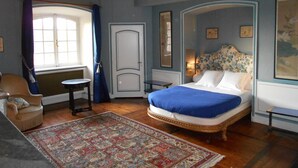 A bedroom with a large bed, a chair, a small table, and a window with curtains. - Château d'Ailly (Parigny)
