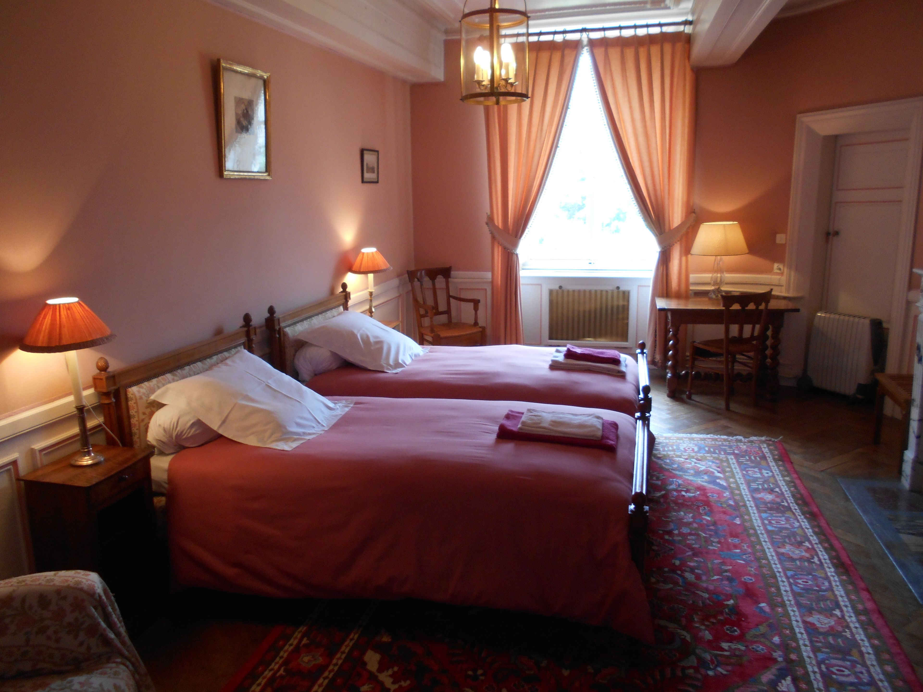A hotel room with two beds, a desk, a chair, and a radiator.