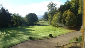 A landscaped garden with a paved path leading to a building entrance. - Château d'Ailly (Parigny)