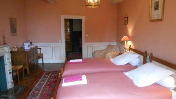 A hotel room with two beds, a desk, a chair, a fireplace, and a chandelier.