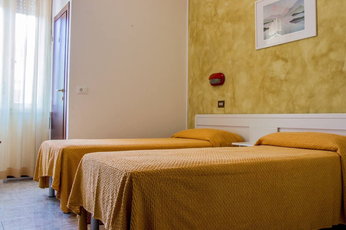 A hotel room with two beds, a painting on the wall, and a red emergency light.