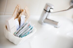 A bathroom sink with a white soap dispenser and a paper towel holder containing cotton pads and a box labeled "Cotton-Free." - Hotel Ulisse (Carpegna)