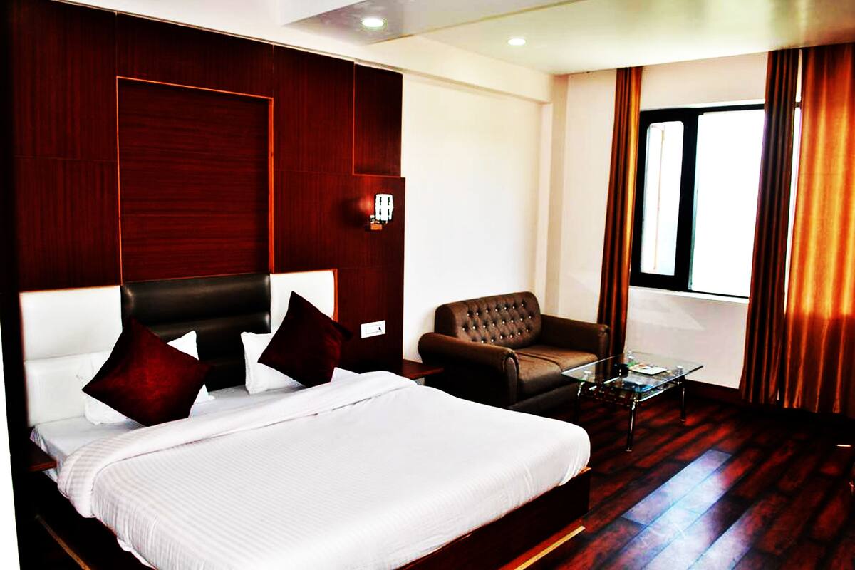 Quarto de hotel com uma cama grande, uma poltrona de couro, uma mesa de centro de vidro e vista para o exterior pela janela.