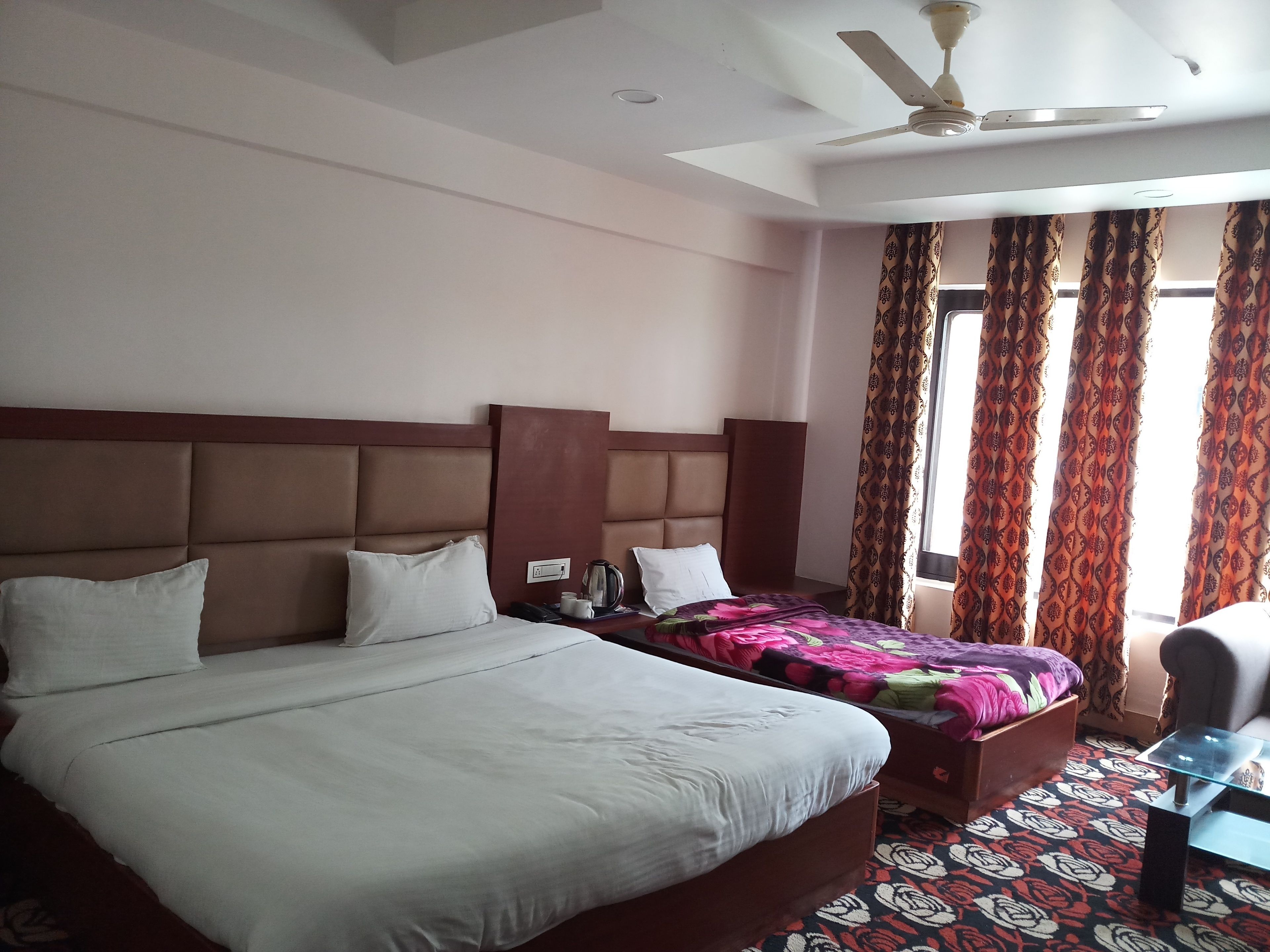 Habitación de hotel con dos camas, un ventilador de techo y cortinas estampadas.