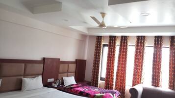 A hotel room with two beds, a sofa, a ceiling fan, and patterned curtains.