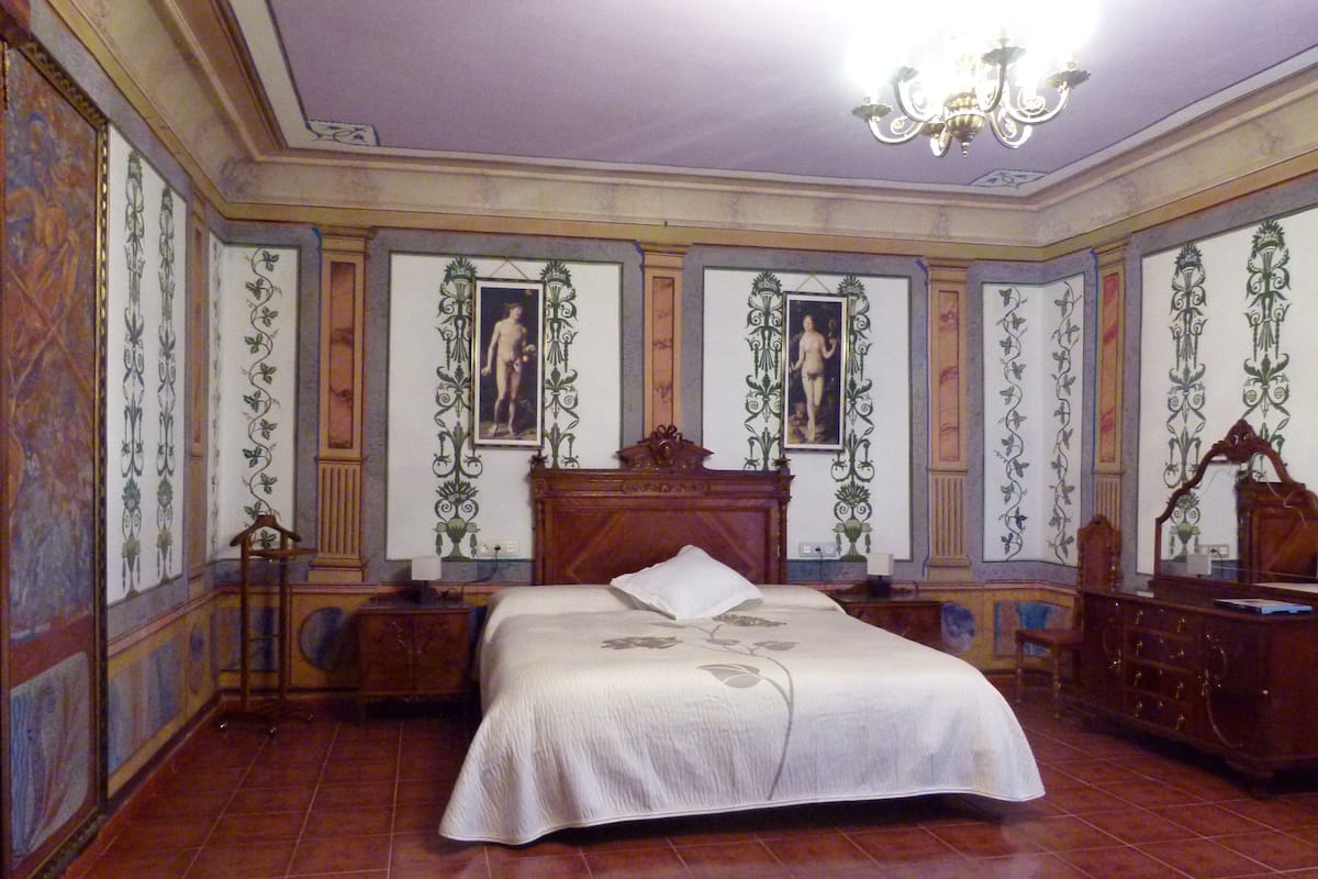 Un dormitorio con una cama grande, un papel tapiz decorativo y una araña.