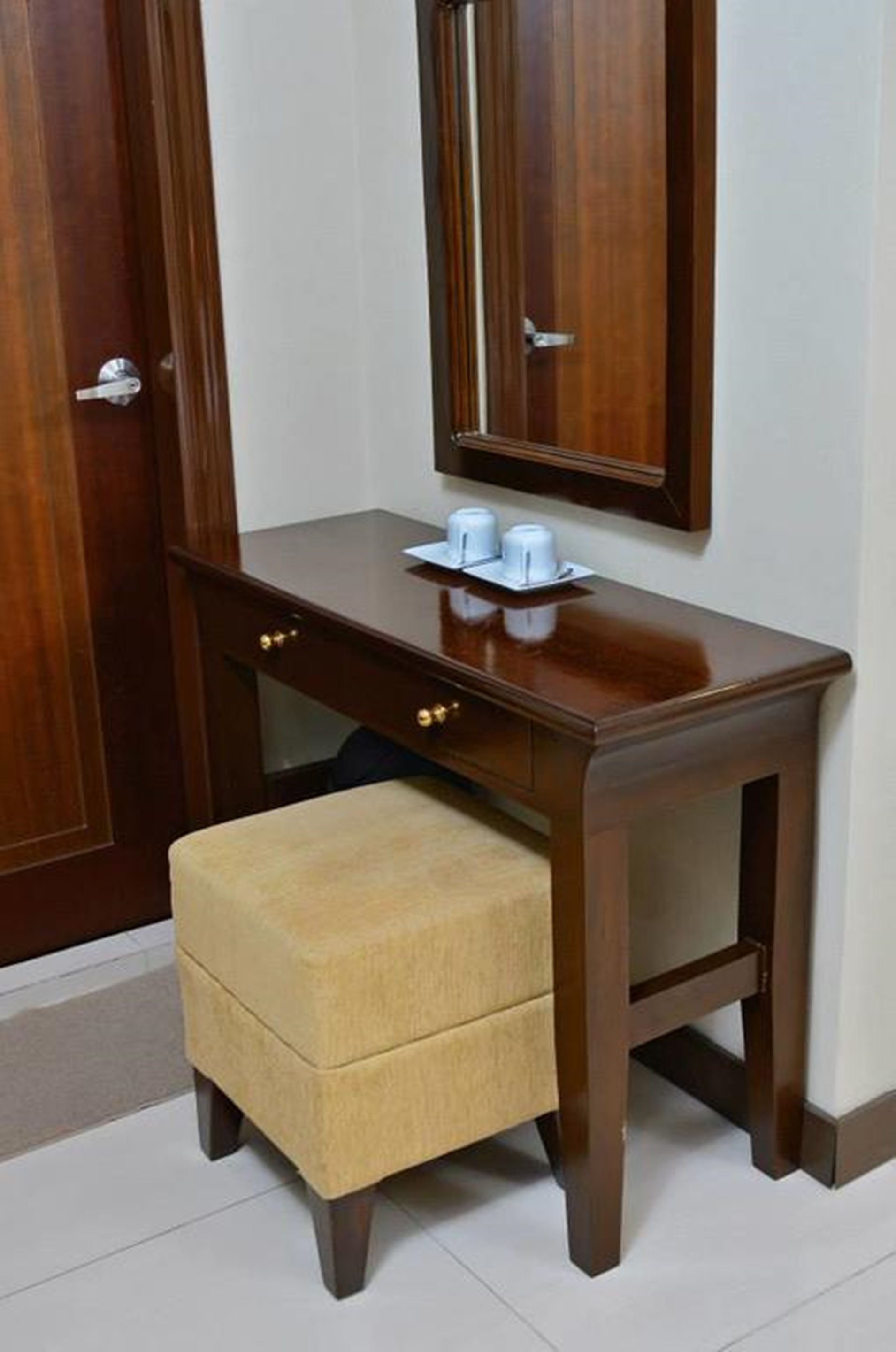 A wooden desk with a mirror, a small stool, and a tray with cups.