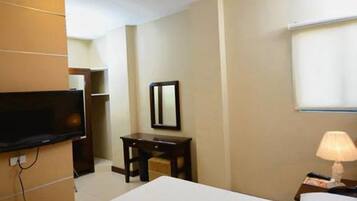 Quarto de hotel com cama, escrivaninha, televisão e luminária.