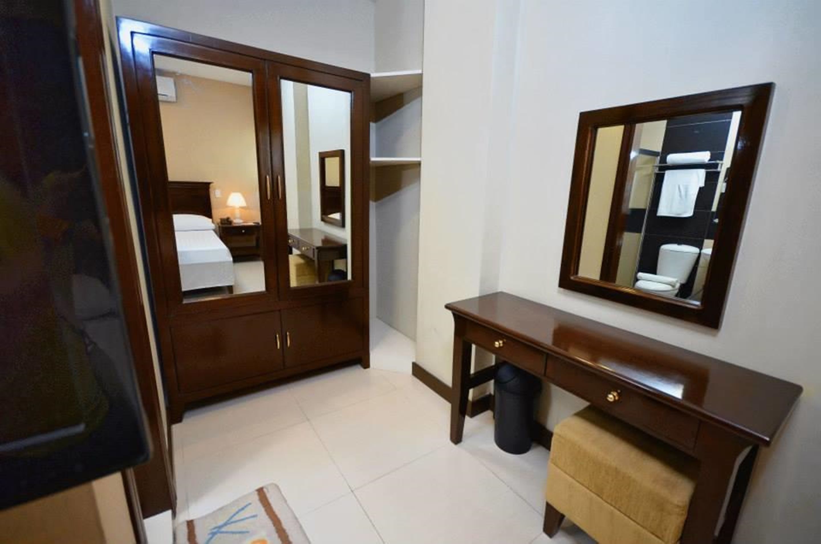 Habitación de hotel con armario, tocador con espejo, pequeña mesa y cubo de basura.