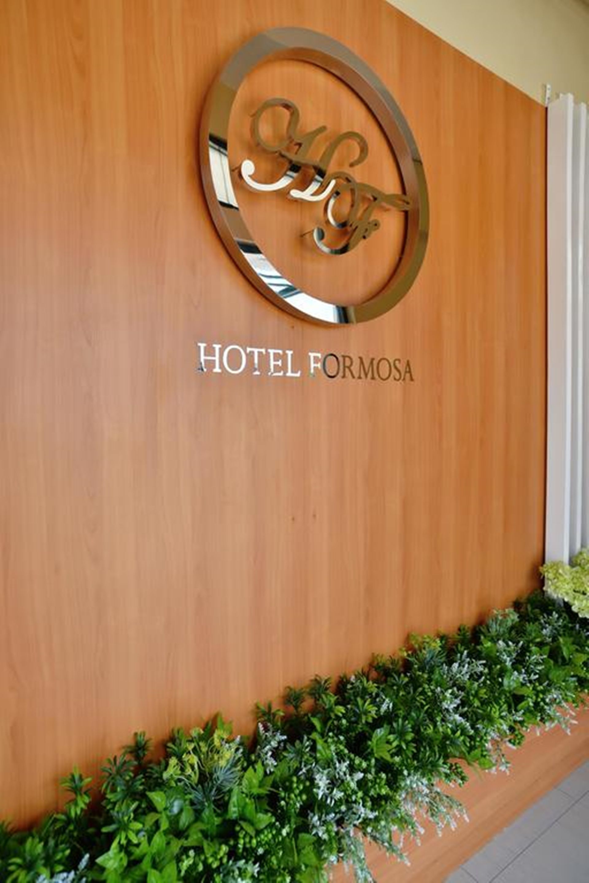 A wooden wall with a circular sign reading "HOTEL FORMOSA" and a green plant border.