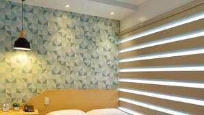 A modern bedroom with a wooden bed, a nightstand, a lamp, and geometric patterned wallpaper.