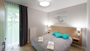 Una habitación de hotel moderna con una cama grande, dos mesitas de noche, un cabecero y un ventanal con cortinas.