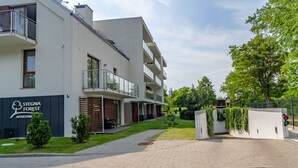 Un moderno edificio de apartamentos con balcones, un jardín ajardinado y una entrada pavimentada.