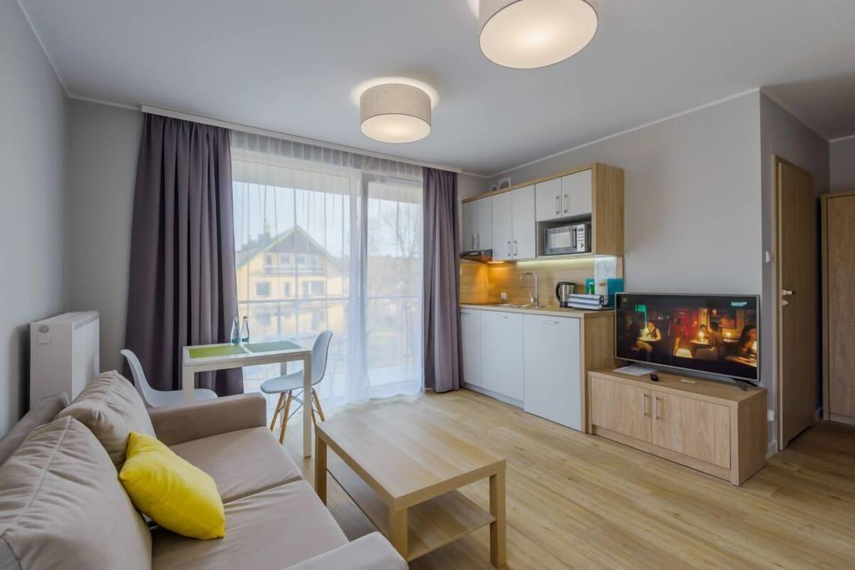A modern living room with a sofa, a dining table, a TV, and a kitchen area.