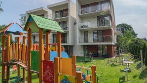 Un parque infantil con juegos de colores y un edificio de varios pisos con balcones al fondo.