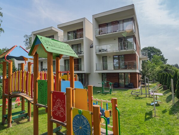 Un parque infantil con juegos de colores y un edificio de varios pisos con balcones al fondo.