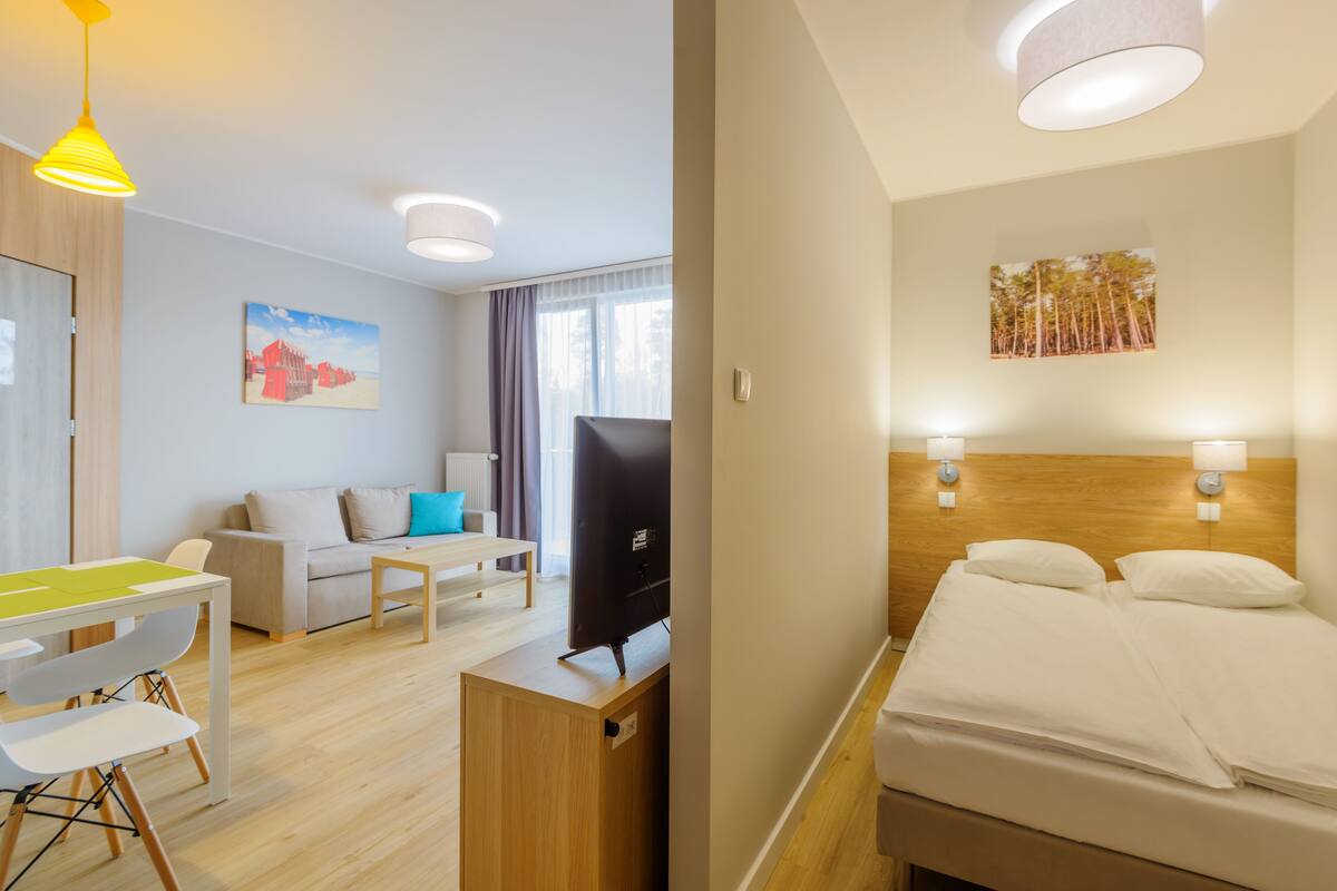 A hotel room with a bed, a desk with a chair, a television, and a painting on the wall.