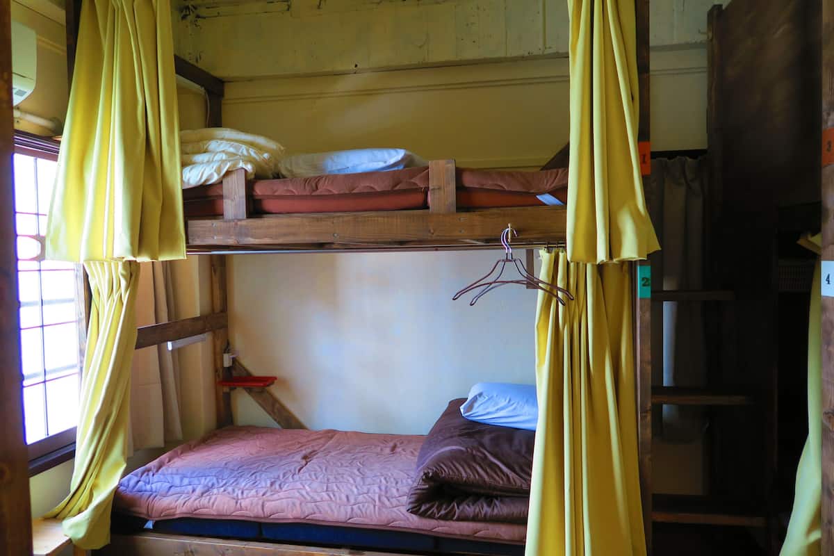 Ein Stockbett mit einer unteren Liege, einem Fenster mit Vorhängen und einer Holzleiter.