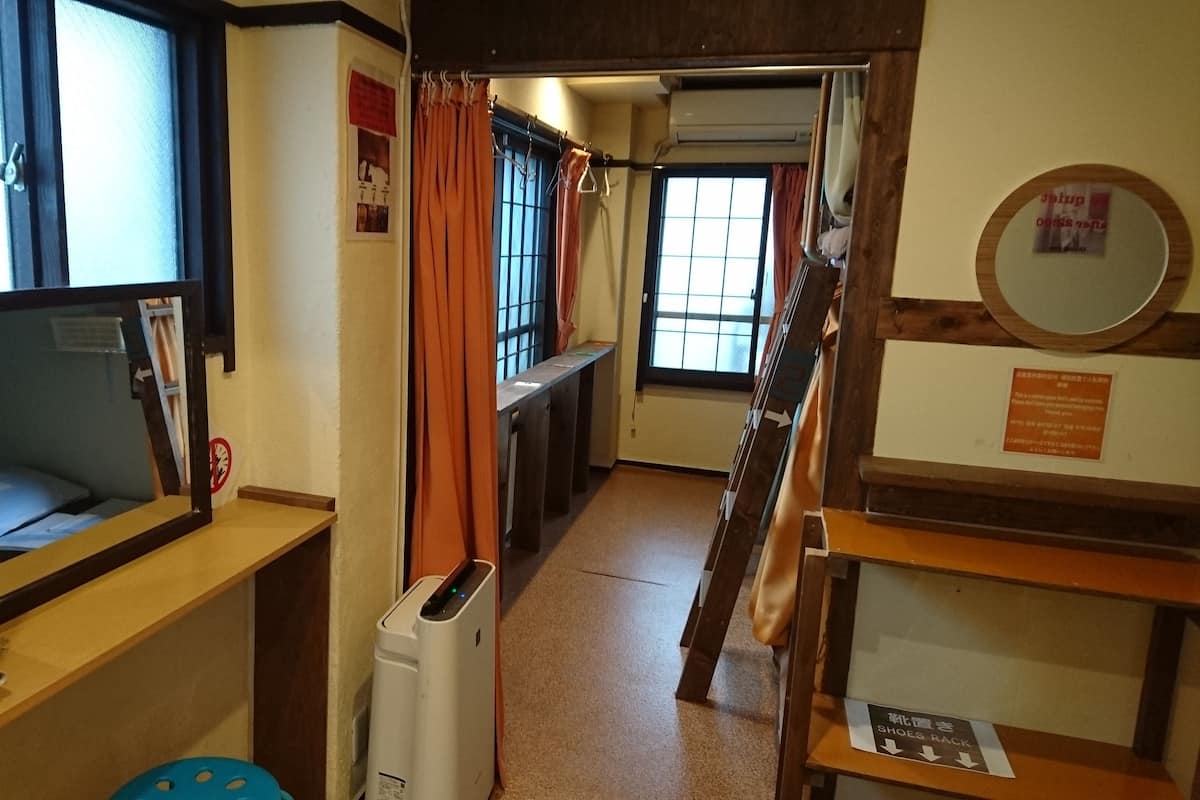 Ein schmaler Gang mit einem Fenster links, einem Spiegel an der linken Wand, einem Heizkörper in der Mitte und einem Schuhregal rechts.