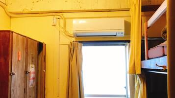 Quarto pequeno com beliche, ventoinha no teto, ar condicionado e janela com cortinas.