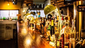 A bar with a wooden counter, various bottles of alcohol, and a green lamp. - Takamatsu Guesthouse BJ Station (Takamatsu)