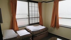 A room with two beds, a window with orange curtains, and a small table. - Takamatsu Guesthouse BJ Station (Takamatsu)