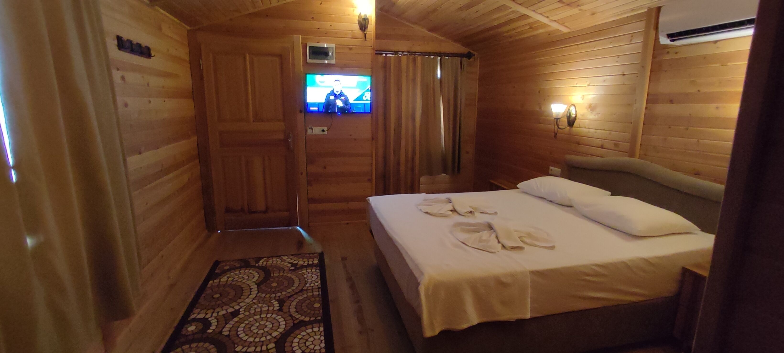 Ein Zimmer in einer Holzhütte mit einem Bett, einem Fernseher und einem gemusterten Teppich.