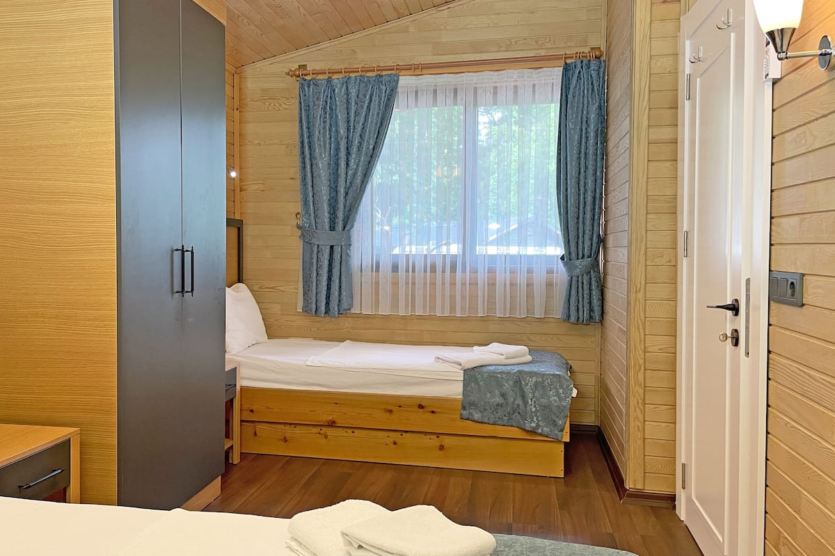 A wooden cabin room with a bed, a small table, and a wardrobe.