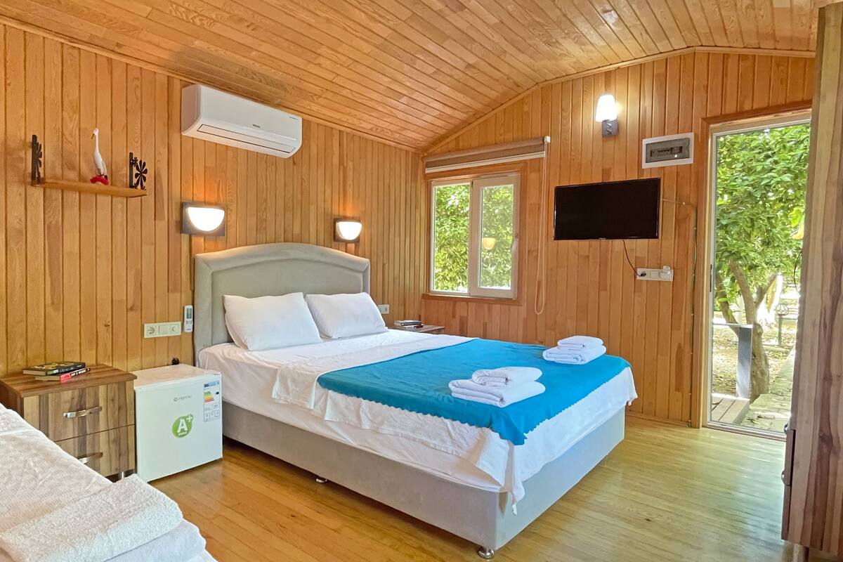 A wooden-paneled room with a bed, bedside table, and a small white cabinet.