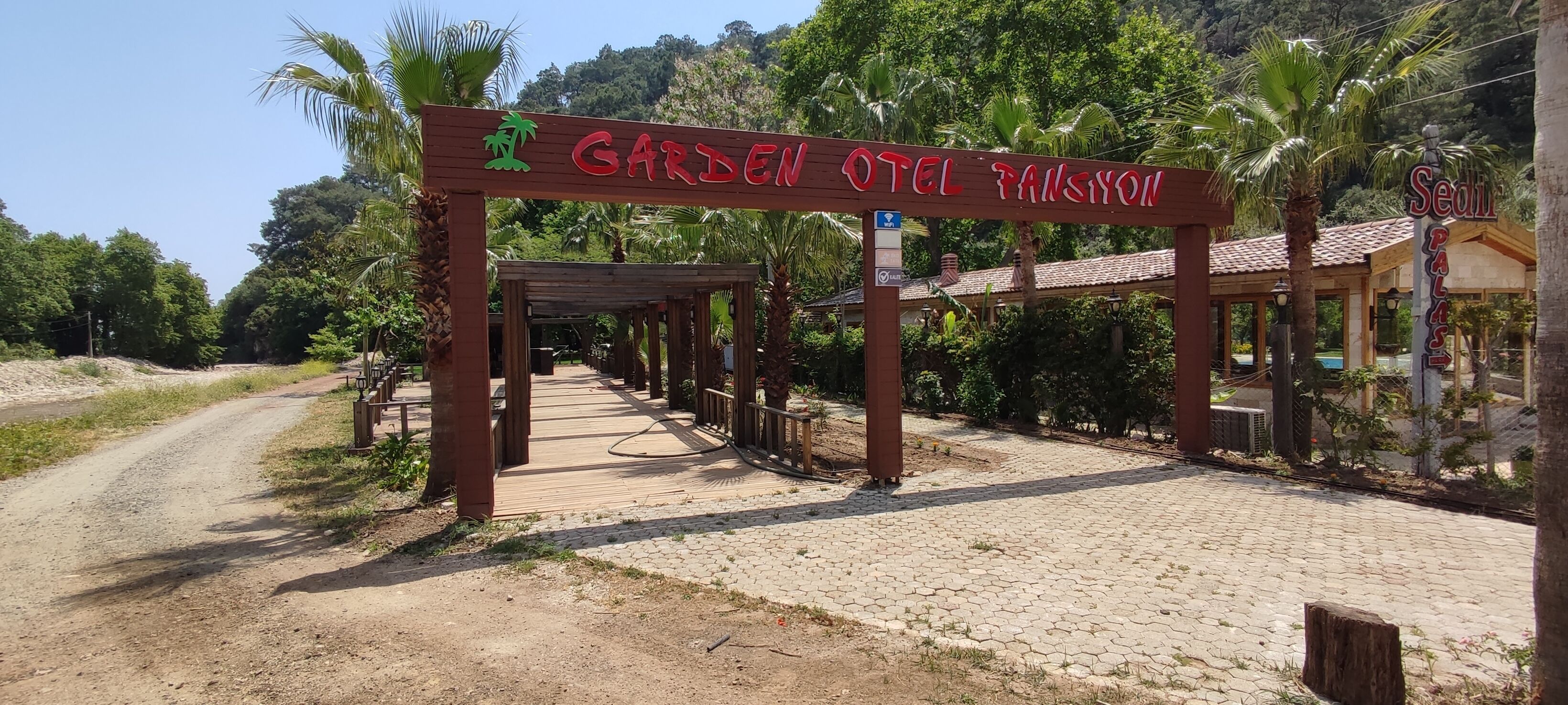 A wooden archway with the text "Garden Hotel Fansiyon" and a palm tree symbol.