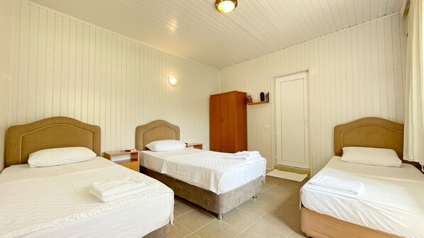 A hotel room with three single beds, a wooden wardrobe, and a door. - Garden Pansiyon (Kemer)