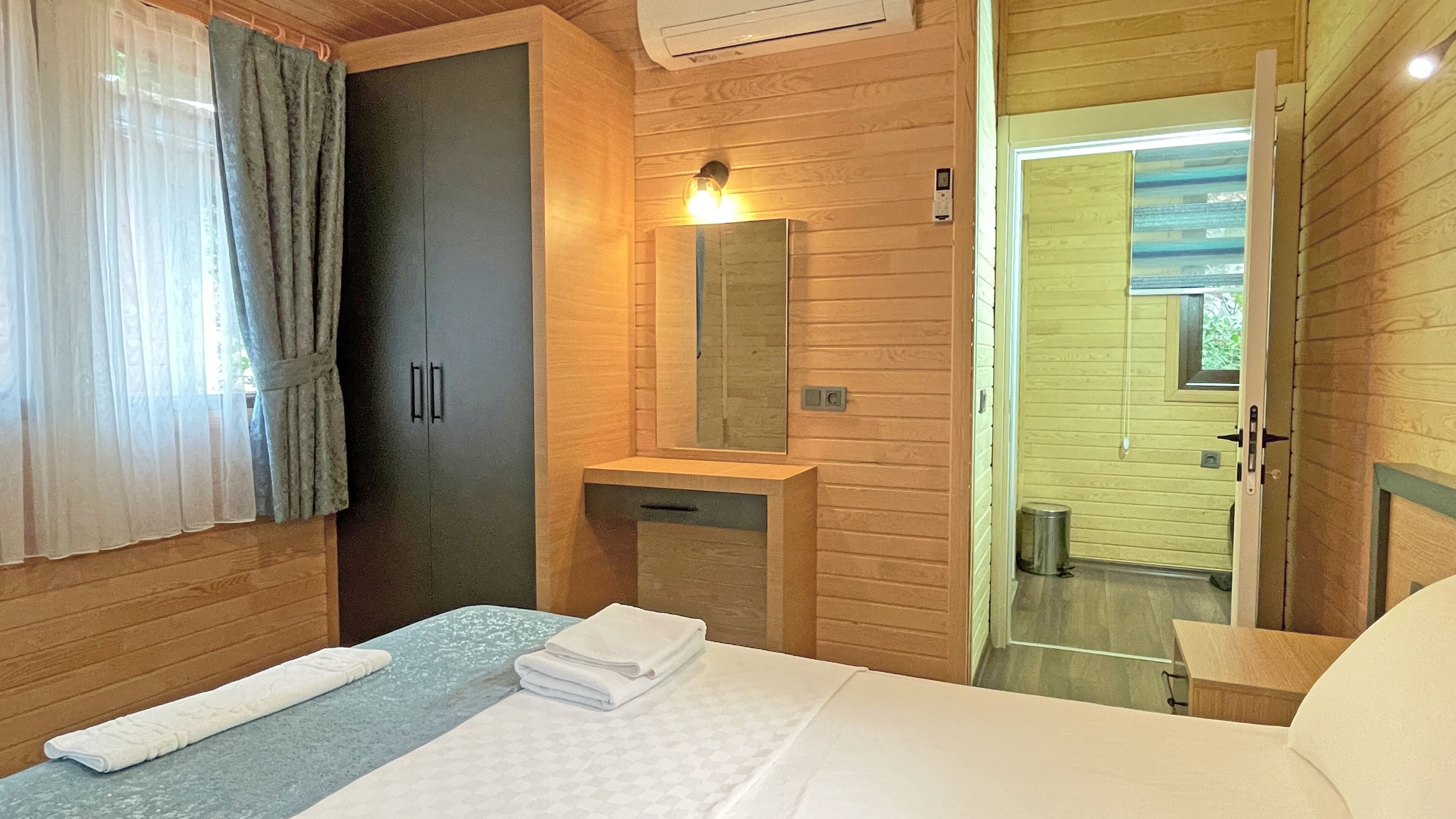 A bedroom with a bed, a bedside table, a mirror, a wardrobe, and a bathroom visible through an open door.