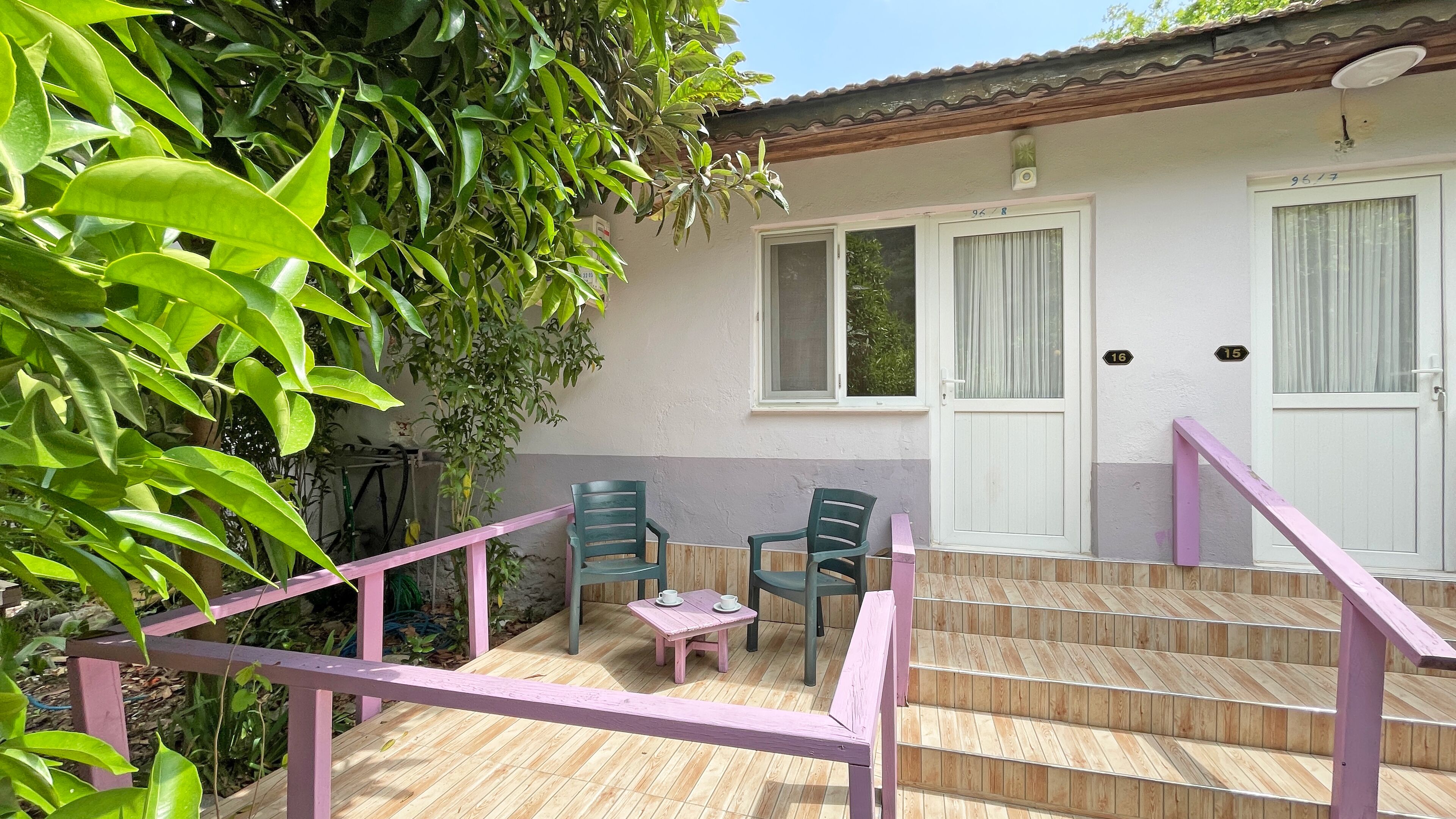 A wooden deck with a pink railing, two green chairs, and a small table with cups.