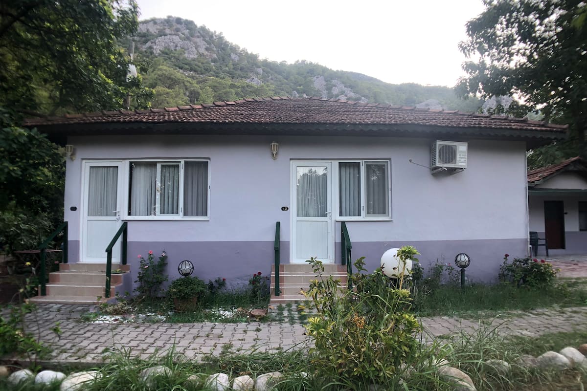 A two-story house with a tiled roof, a front porch, and a garden with potted plants and a small statue.