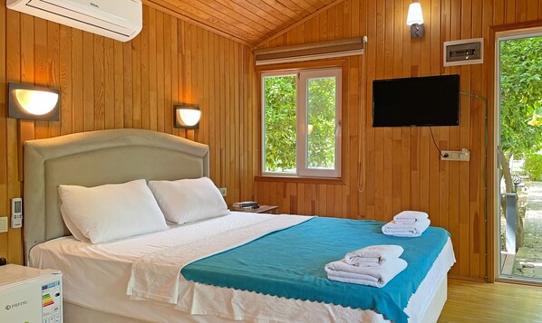 A hotel room with a bed, a TV, a window, and a wall-mounted air conditioner.