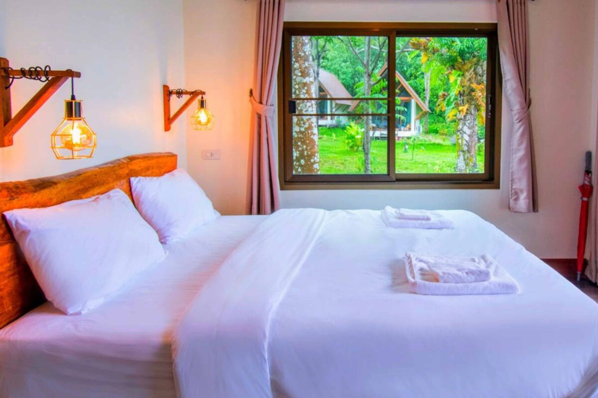 Una camera d'albergo con un letto grande, una finestra vista giardino e una testiera in legno.