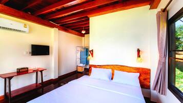 A bedroom with a wooden ceiling, a bed with white linens, a TV mounted on the wall, and a window with curtains.