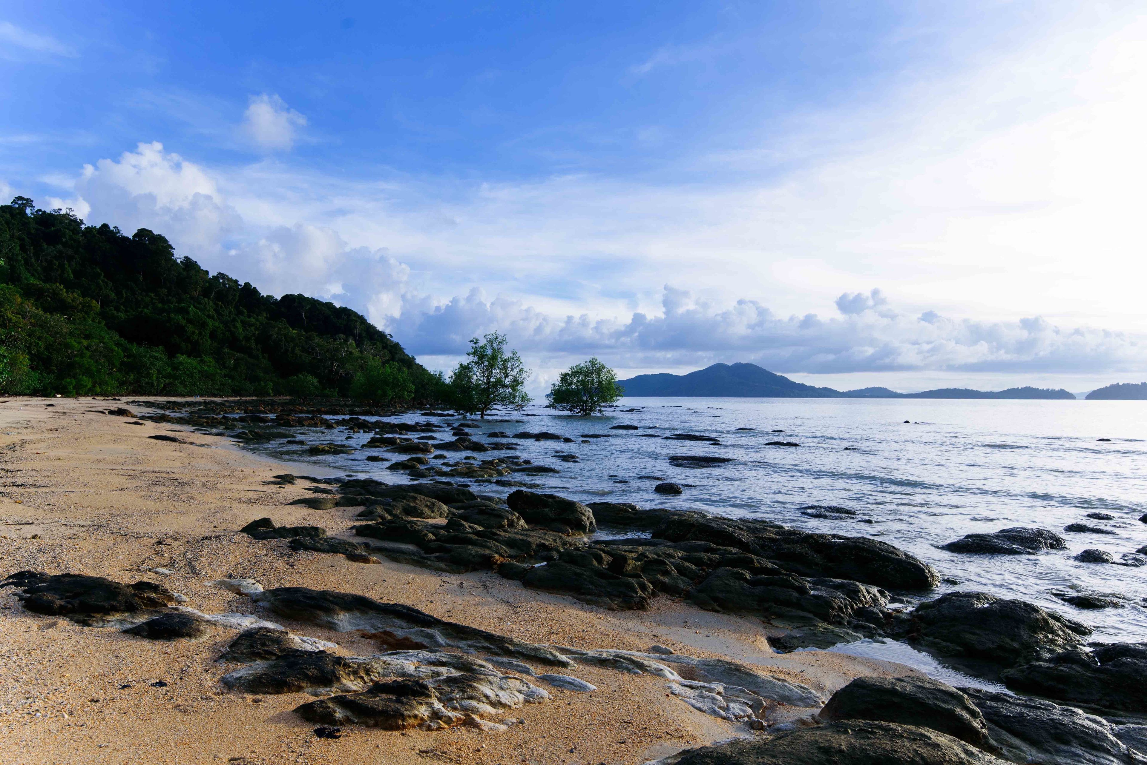 A beach with rocky shoreline, clear blue sky, and distant mountains.