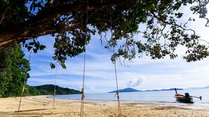 Une plage avec une balançoire, un bateau et une zone boisée en arrière-plan.