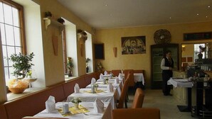 A restaurant with long tables set for dining, a bartender at the bar, and a large window on the left. - Mantra Gästehaus (Dachau)