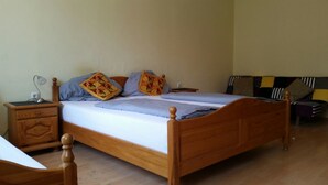A neatly made bed with a wooden frame, a bedside table with a lamp, and a chair. - Mantra Gästehaus (Dachau)