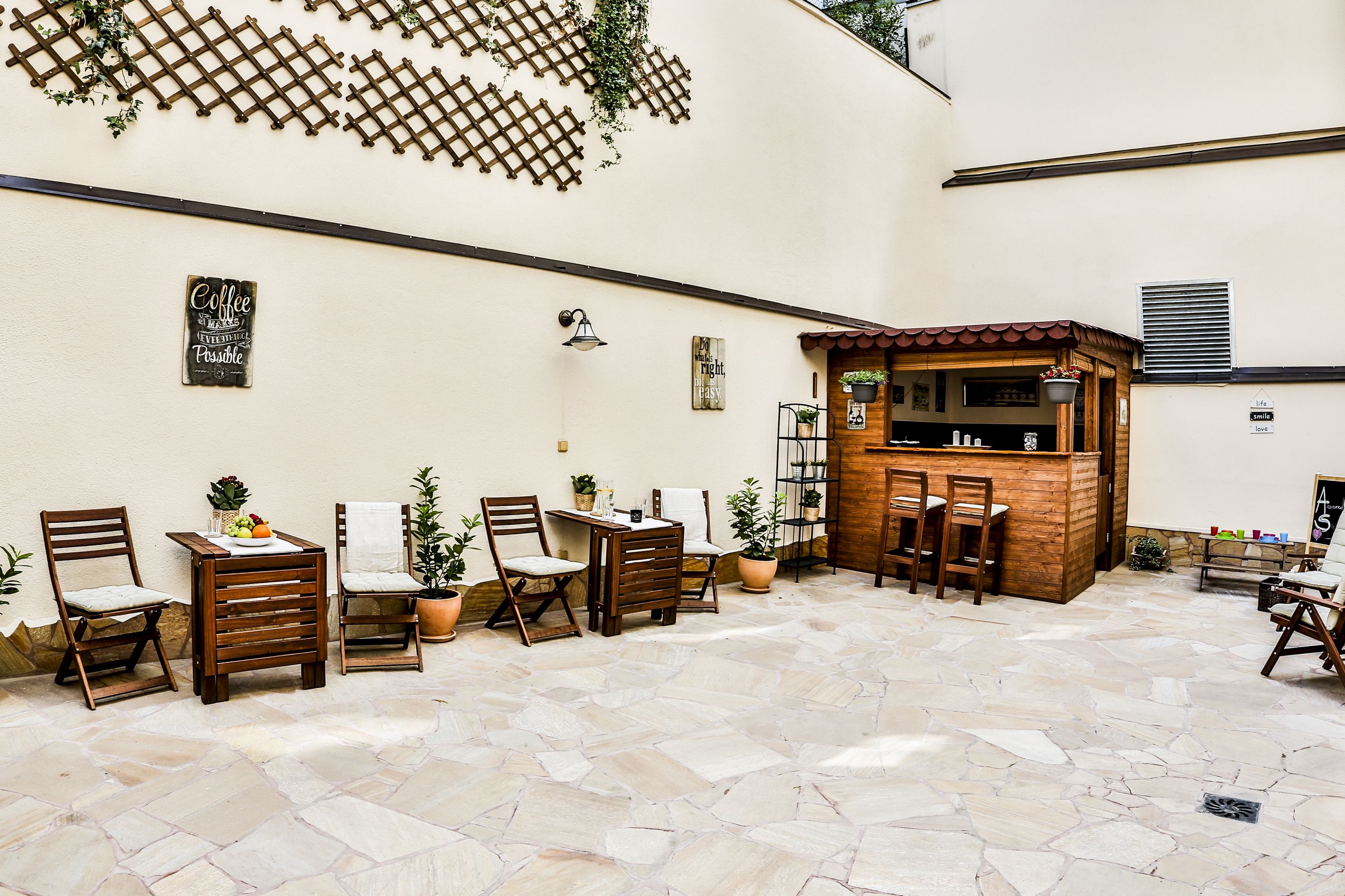 A café with wooden furniture, stone flooring, and a lattice wall with greenery.