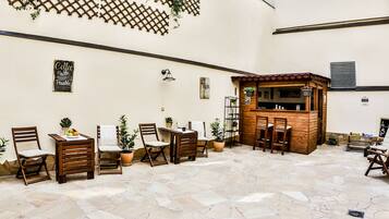 A café with wooden furniture, stone flooring, and a lattice wall with greenery.