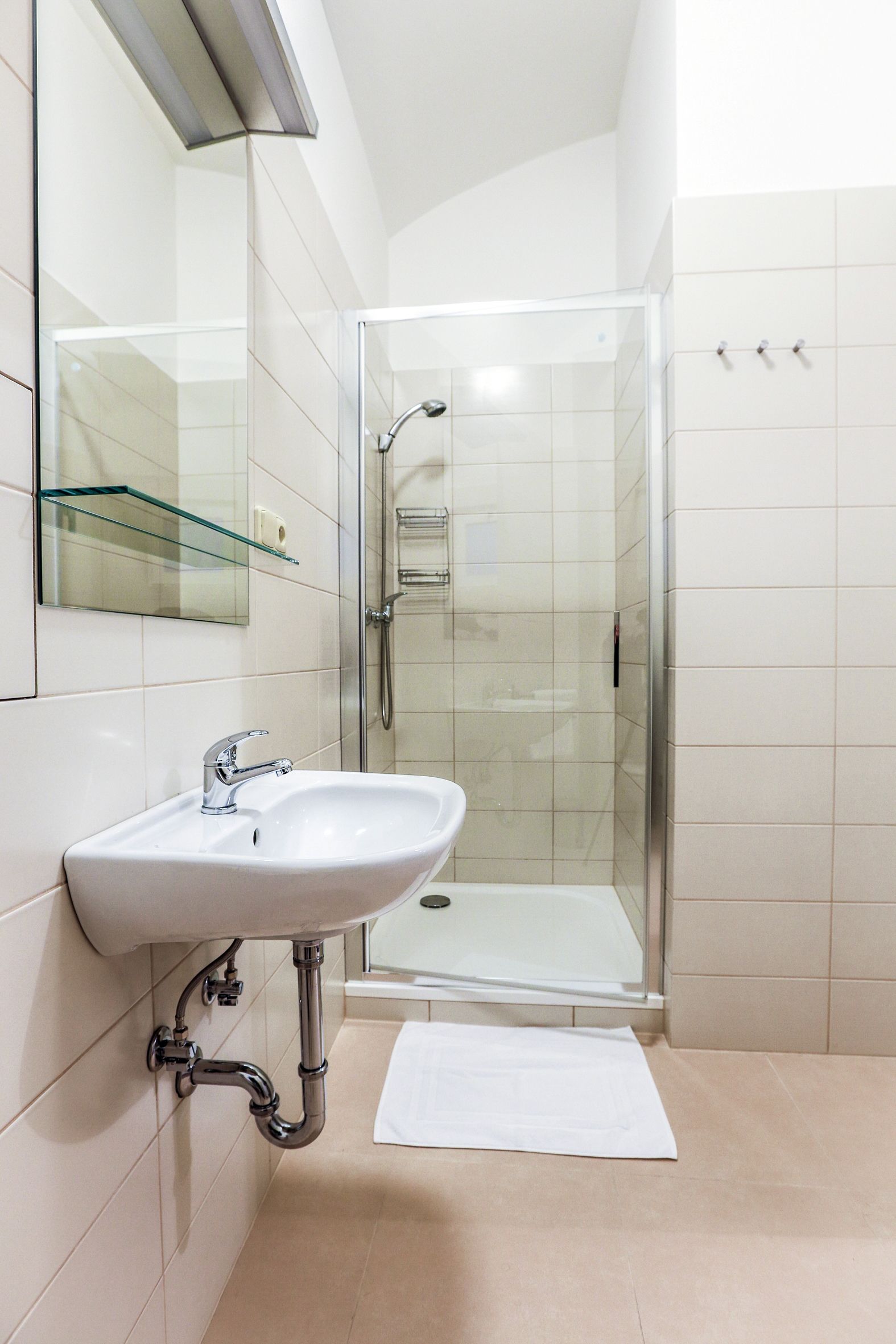 A modern bathroom with a glass shower enclosure, a white sink, and a glass shelf above the mirror.